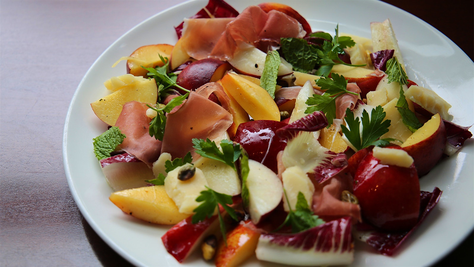  Plate of salad containing peaches, radicchio, prosciutto, aged cheddar, pistachios and mint 